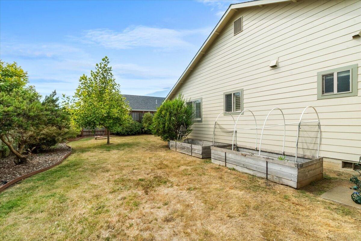Side yard with raised garden beds and hoop frames beside a light-colored house.