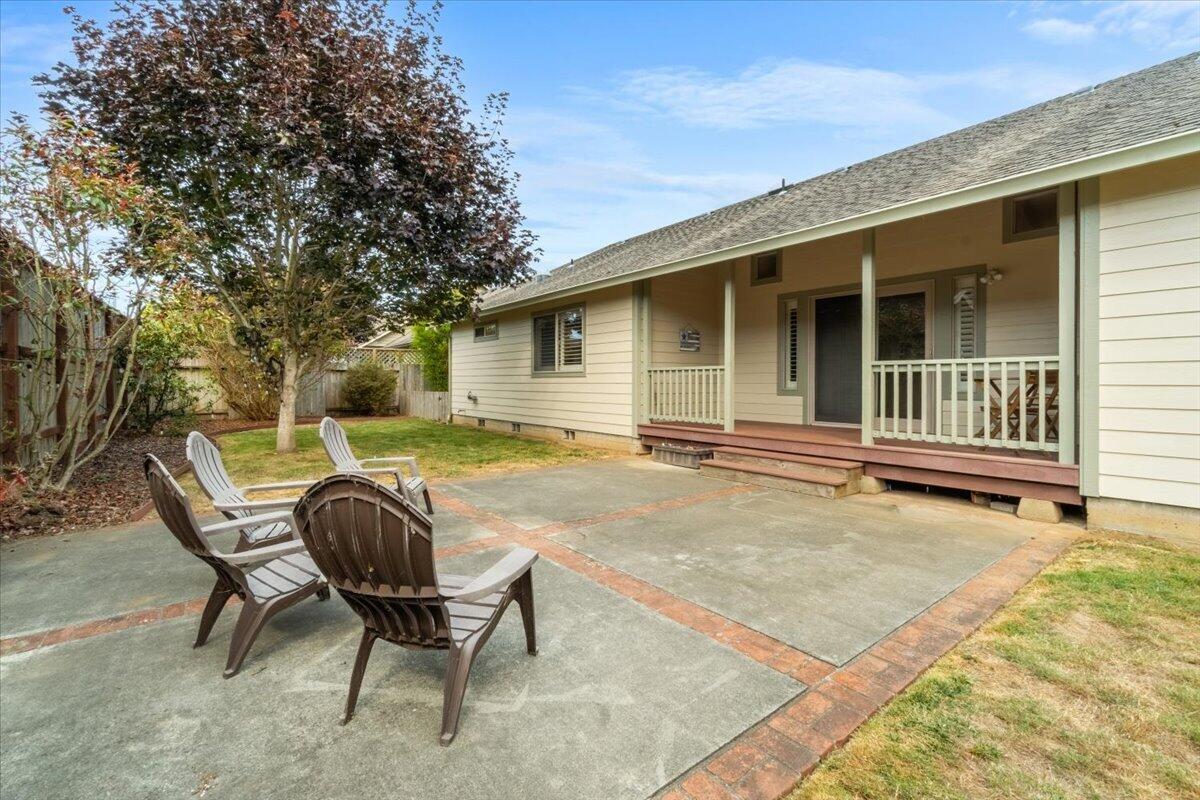 House's covered back porch and brick-bordered concrete patio with chairs beneath a large tree.