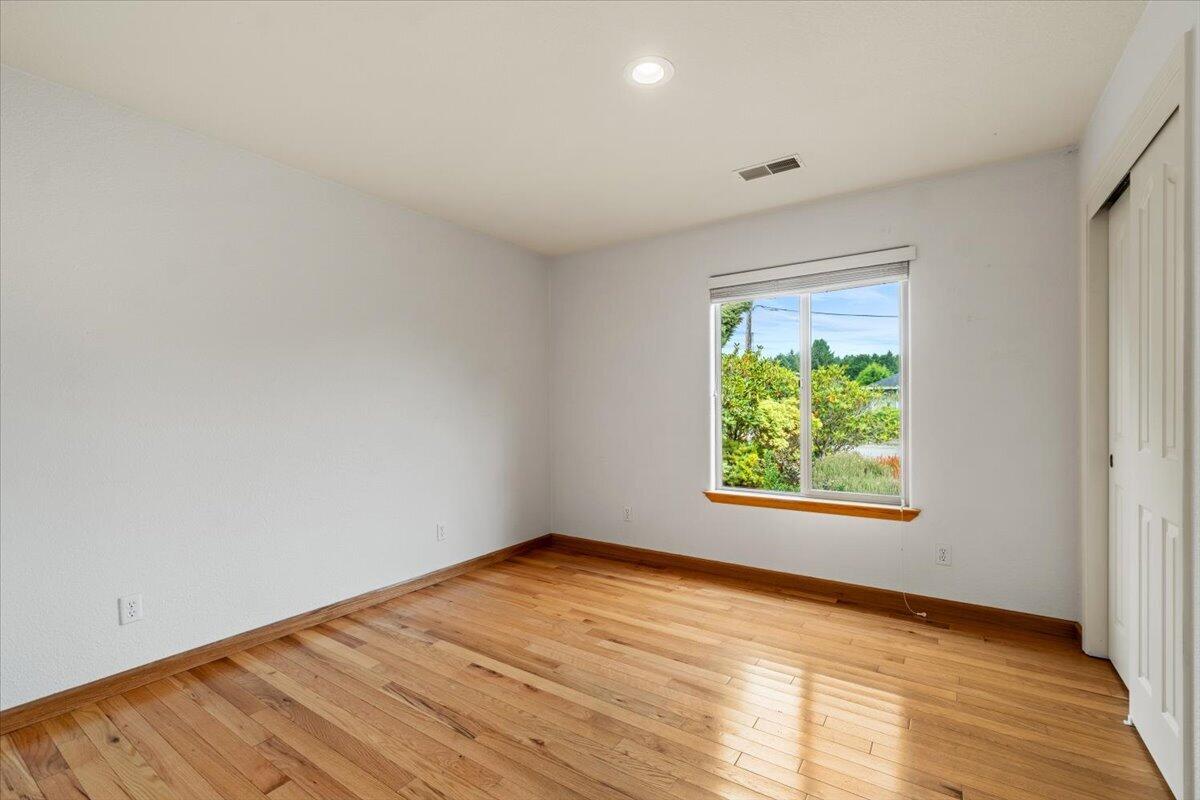Empty bedroom with hardwood floors, a window overlooking greenery, and sliding closet doors.