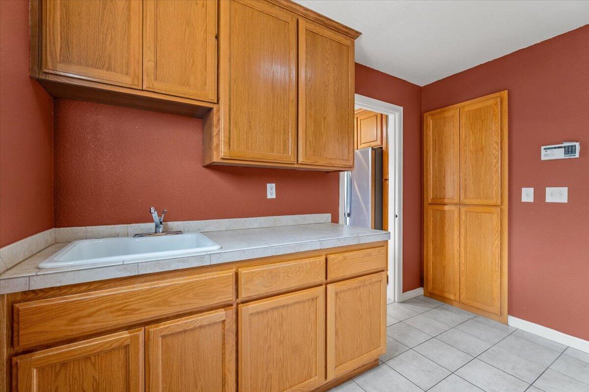 Utility room with a deep sink, oak cabinets, reddish walls, and tile flooring.