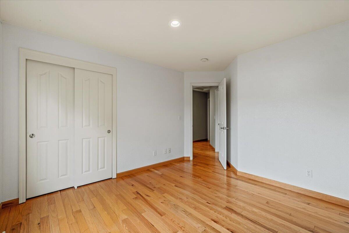 Empty bedroom with hardwood floors, a double-door closet, and an open doorway.