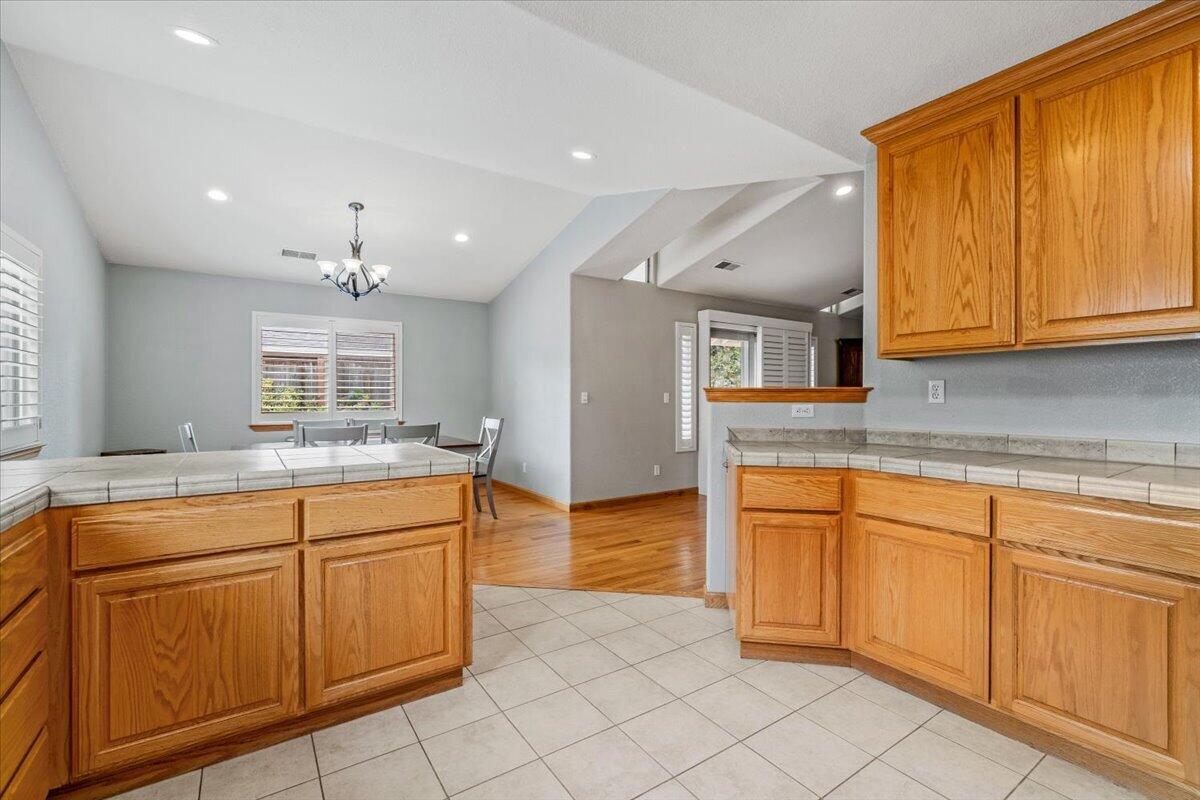 Kitchen opening to a dining area, with warm wood cabinets, tiled counters, and a chandelier.