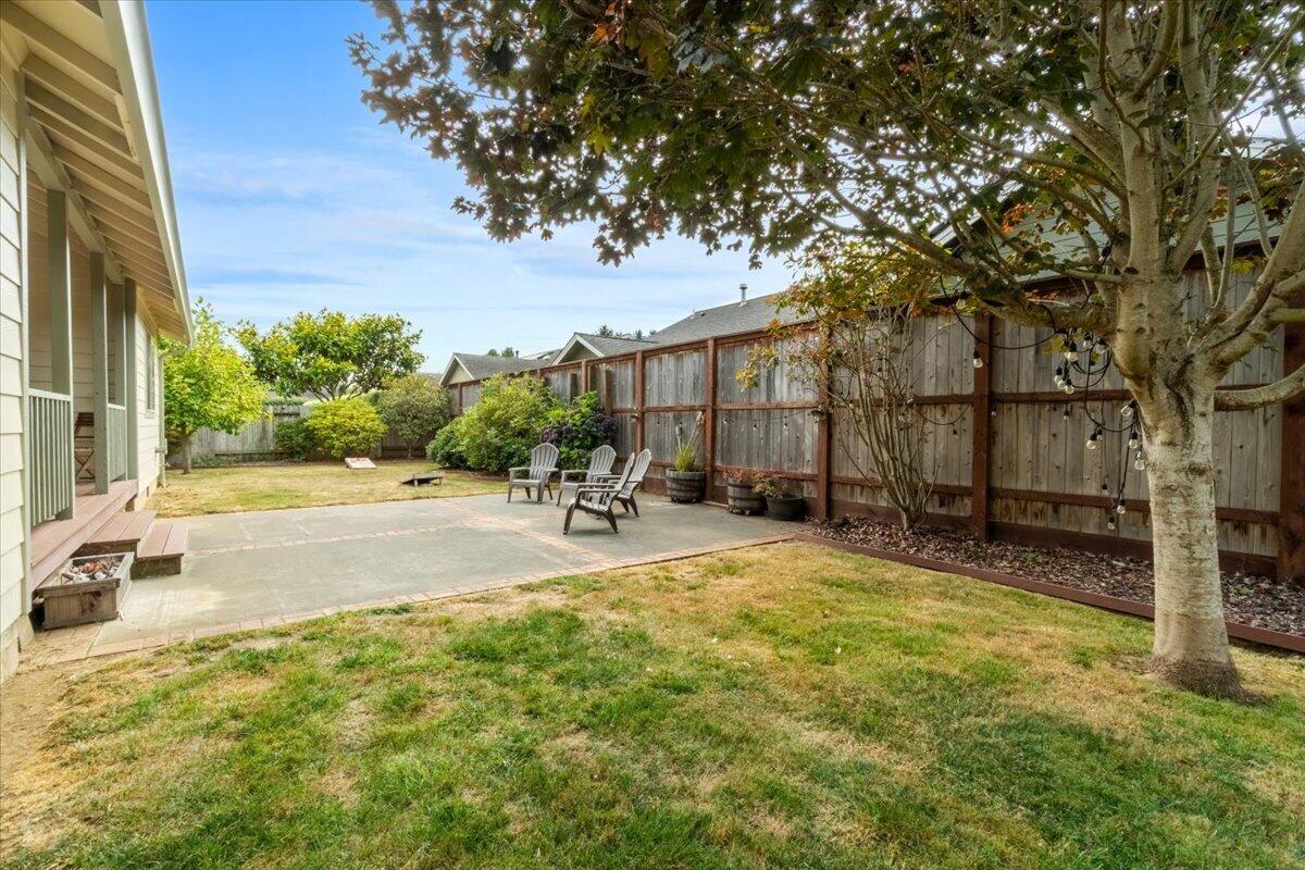 Fenced backyard with a concrete patio, outdoor chairs, and a mature tree.