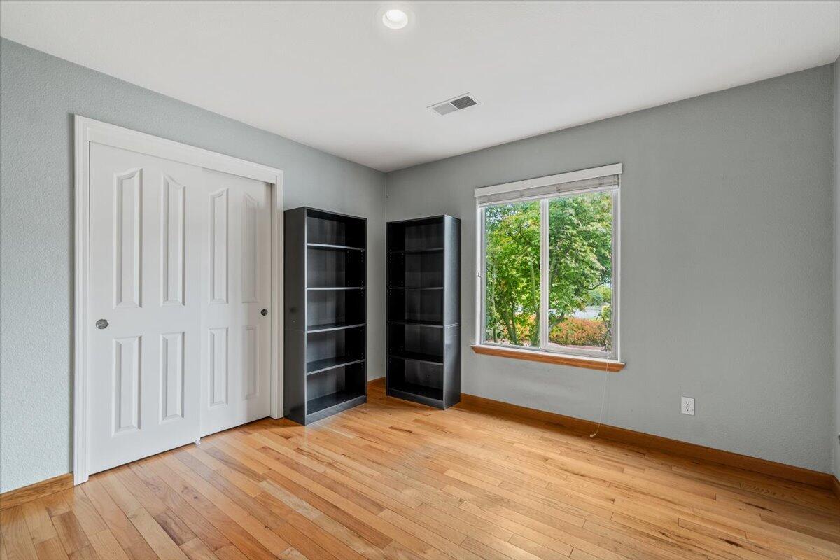Empty bedroom with hardwood floors, white closet doors, and two dark bookcases beside a window.
