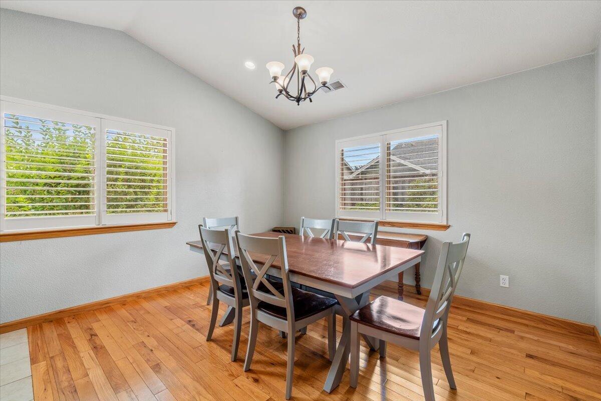 Dining room with a wooden table, gray chairs, plantation shutters, and hardwood floors.