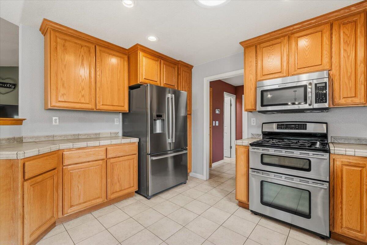 Kitchen with honey-toned wood cabinets, stainless steel appliances, and light tile flooring.