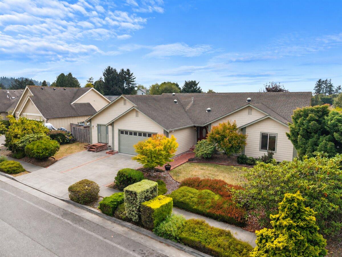 Single-story beige home with an attached garage, wide driveway, and landscaped front garden.