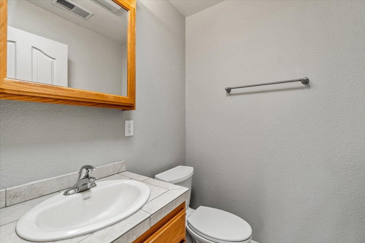 Bathroom with a tiled sink vanity, white toilet, and wood-framed mirror.