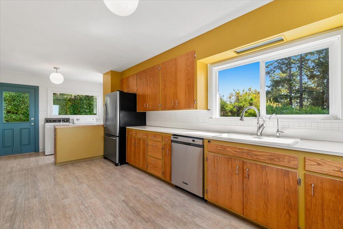 Kitchen with wood cabinets, yellow walls, and a large window overlooking trees.