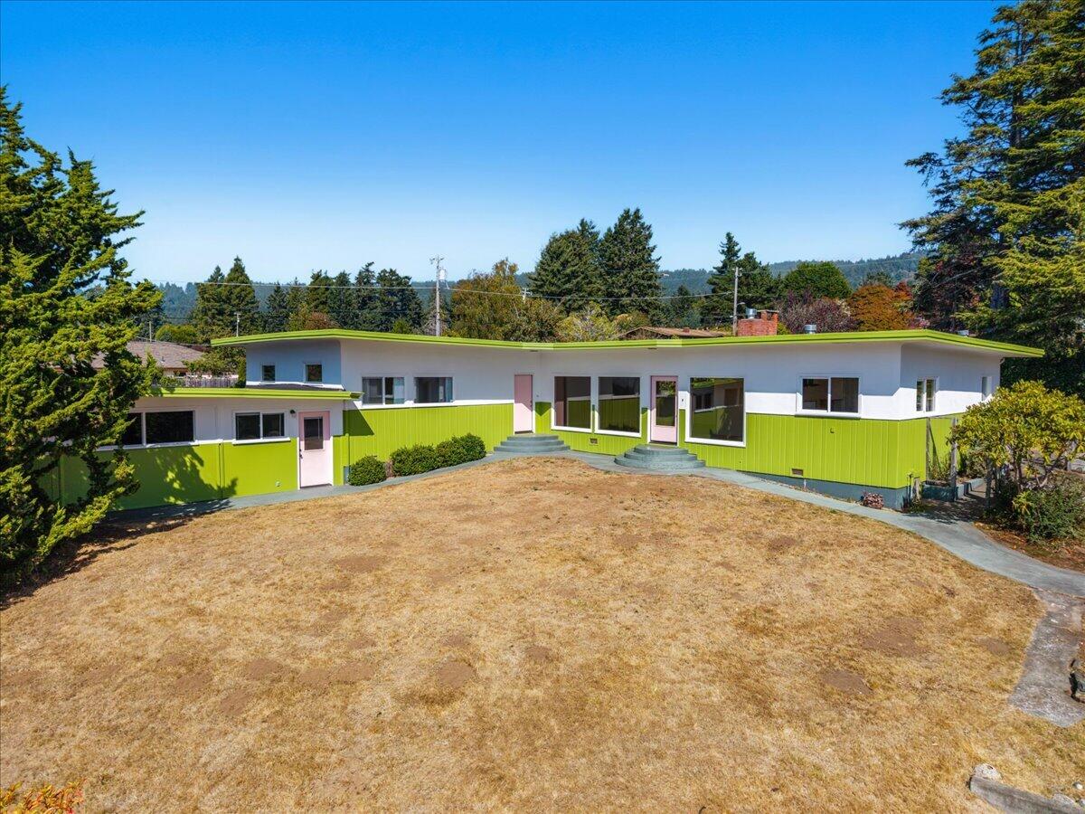 Single-story home with lime-green siding, pink doors, and a broad dry front lawn.