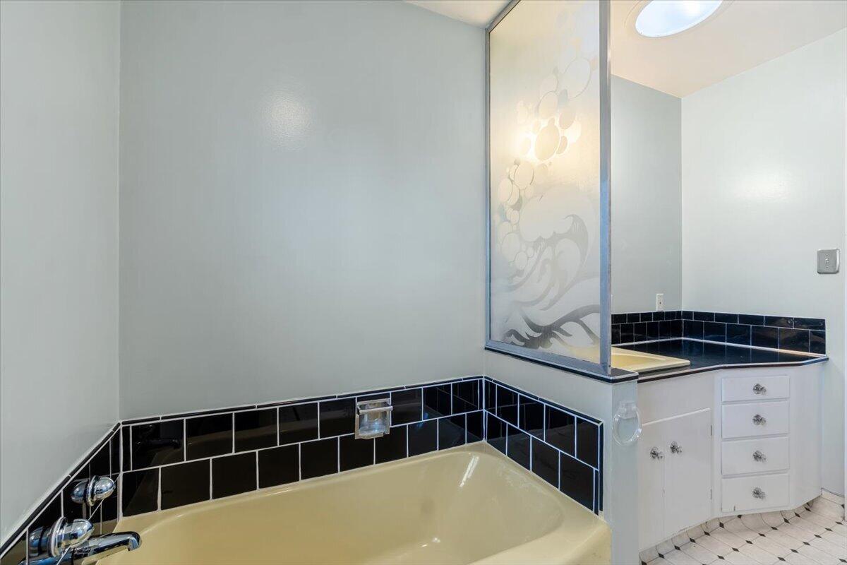 Bathroom with a cream bathtub, black tile surround, frosted glass partition, and white vanity.