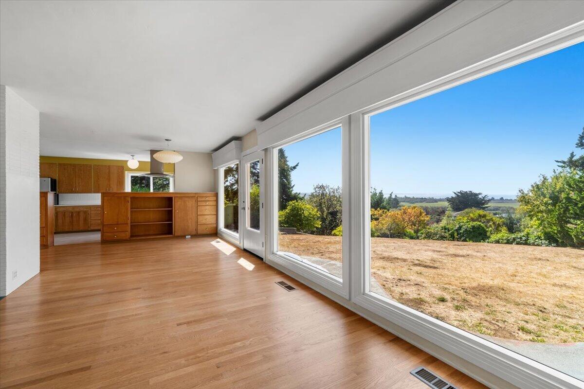 Open living area with wood floors, built-in cabinetry, and expansive windows overlooking the yard.