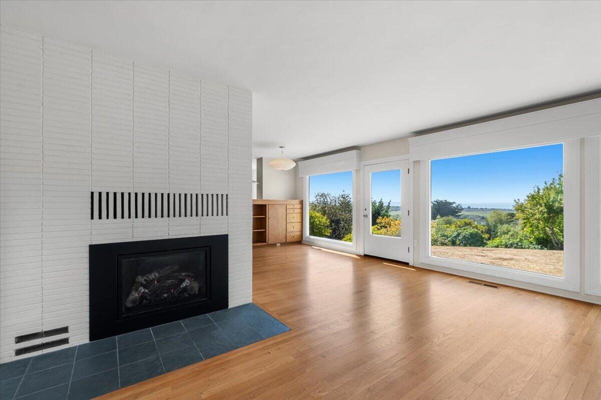 Living room with a white tiled fireplace, wood floors, and large windows overlooking the water.