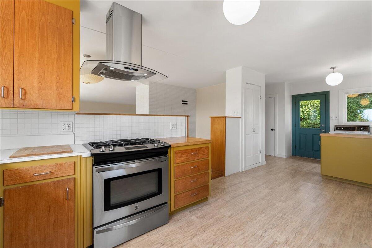 Kitchen with yellow cabinetry, a stainless steel range, and a teal door opening to greenery.