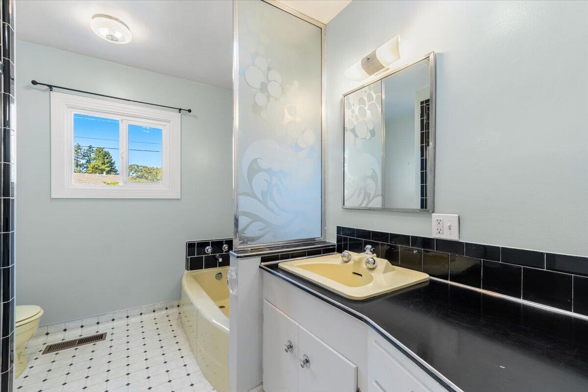 Bathroom with a frosted glass tub partition, black countertop, and window.