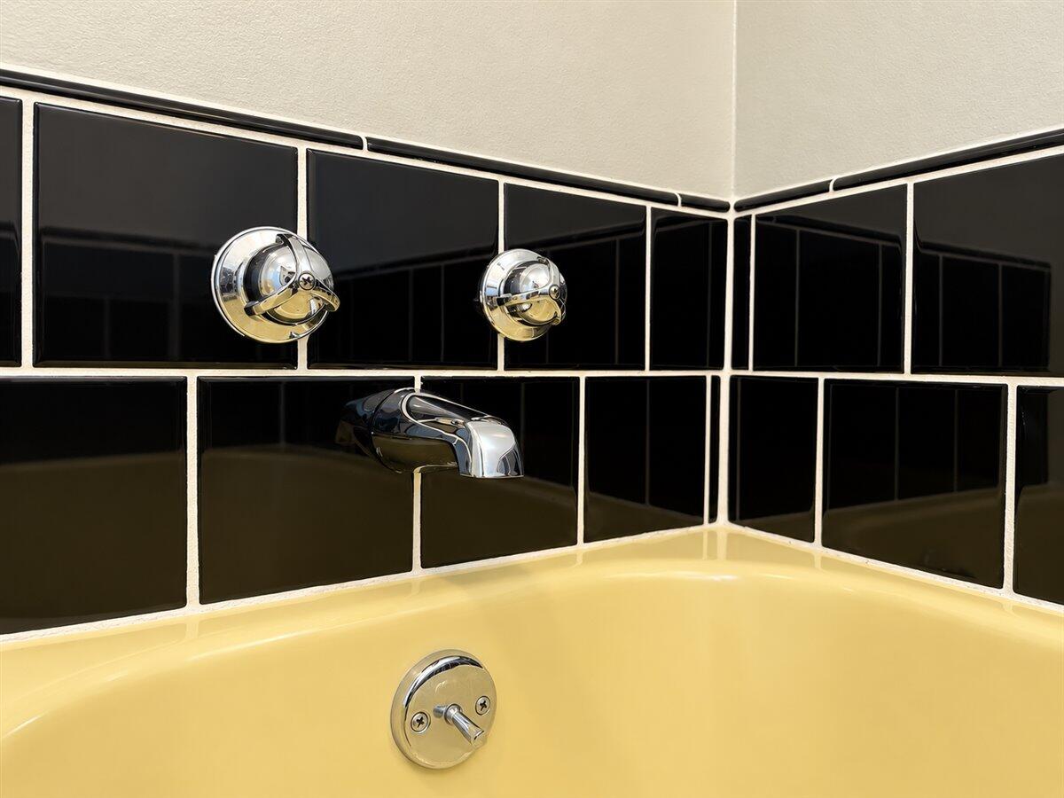 Yellow bathtub with chrome fixtures and glossy black tile surround.