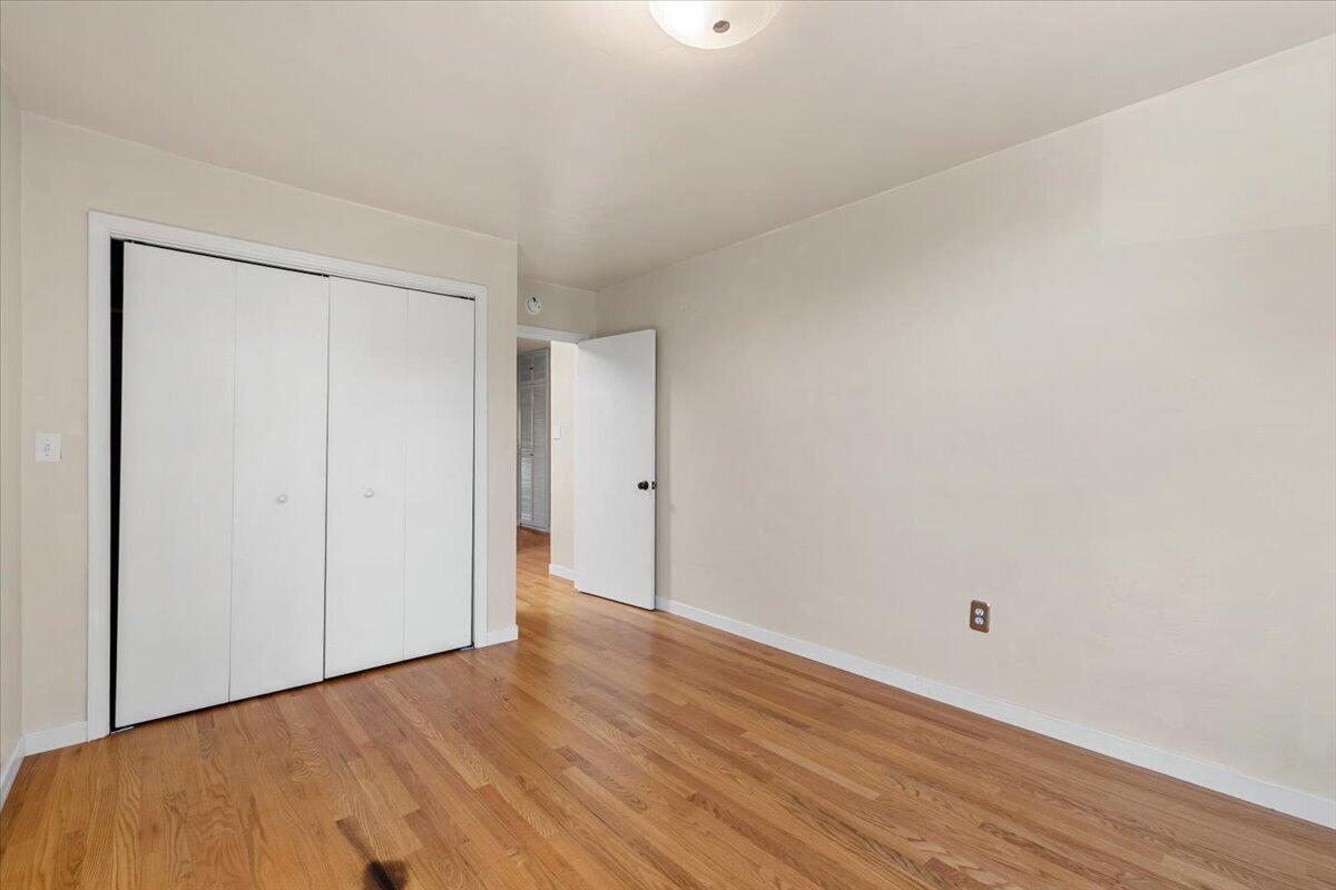 Empty bedroom with wood floors, a white sliding-door closet, and an open doorway.