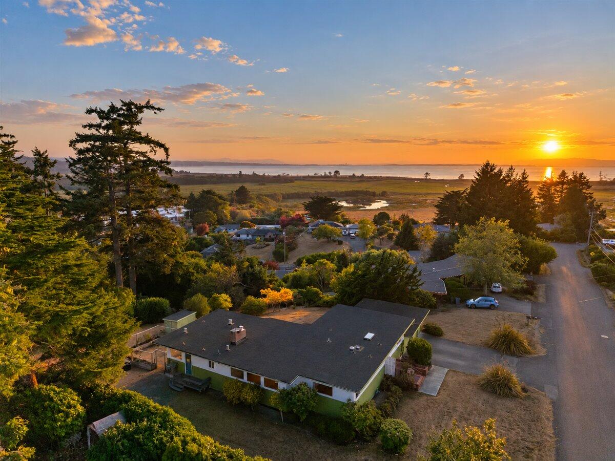 Aerial view of a single-story home with coastal wetlands and water beyond at sunset.