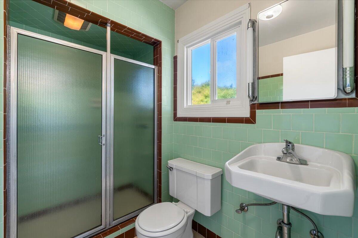 Bathroom with mint-green tile, a frosted-glass shower, white pedestal sink, toilet, and window.