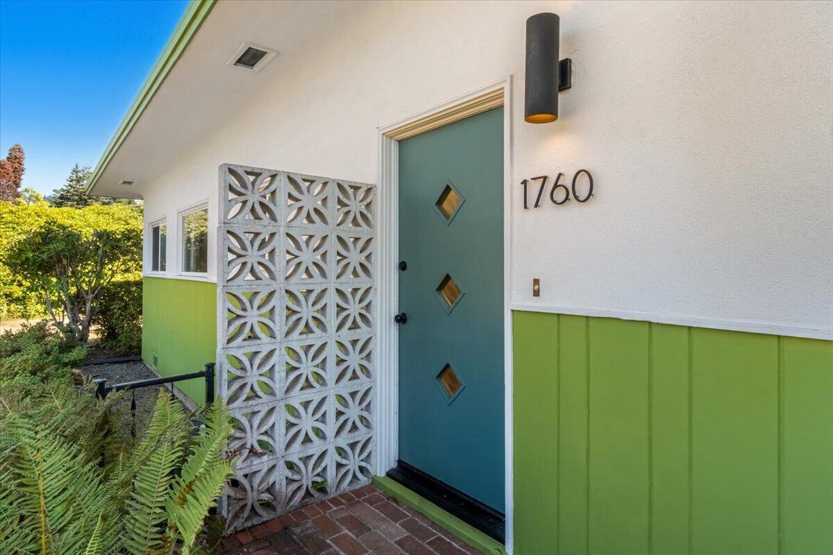 Home entrance with a teal diamond-window door, green siding, patterned concrete screen, and brick walkway.