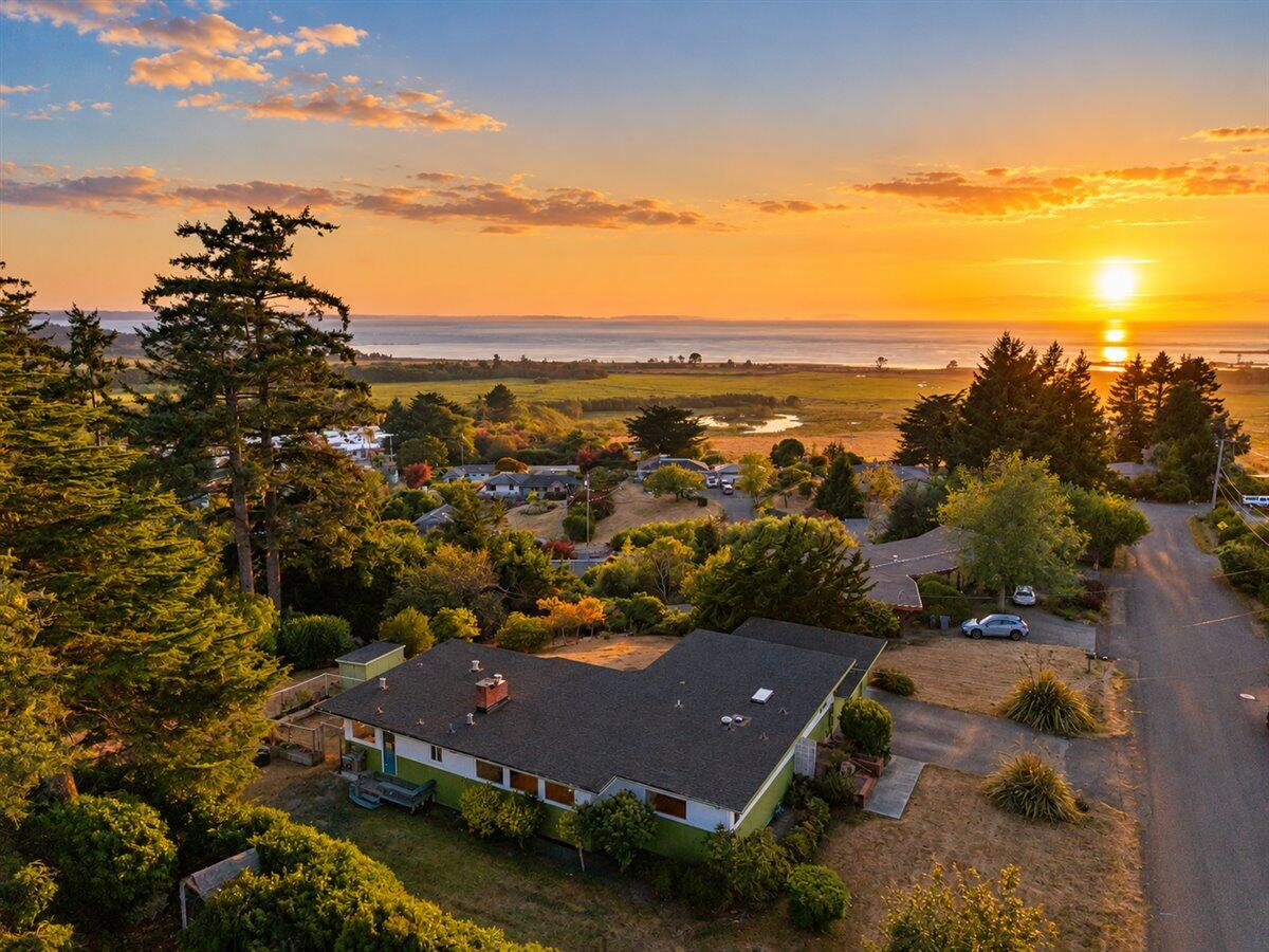 Aerial view of a single-story home with coastal water and sunset in the distance.