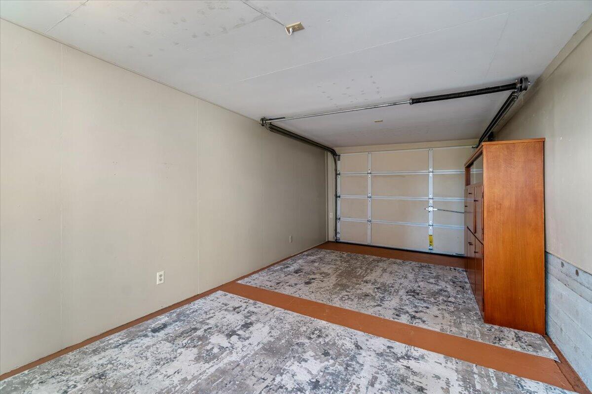 Empty garage with a closed sectional door, worn patterned floor covering, and a tall wooden cabinet.