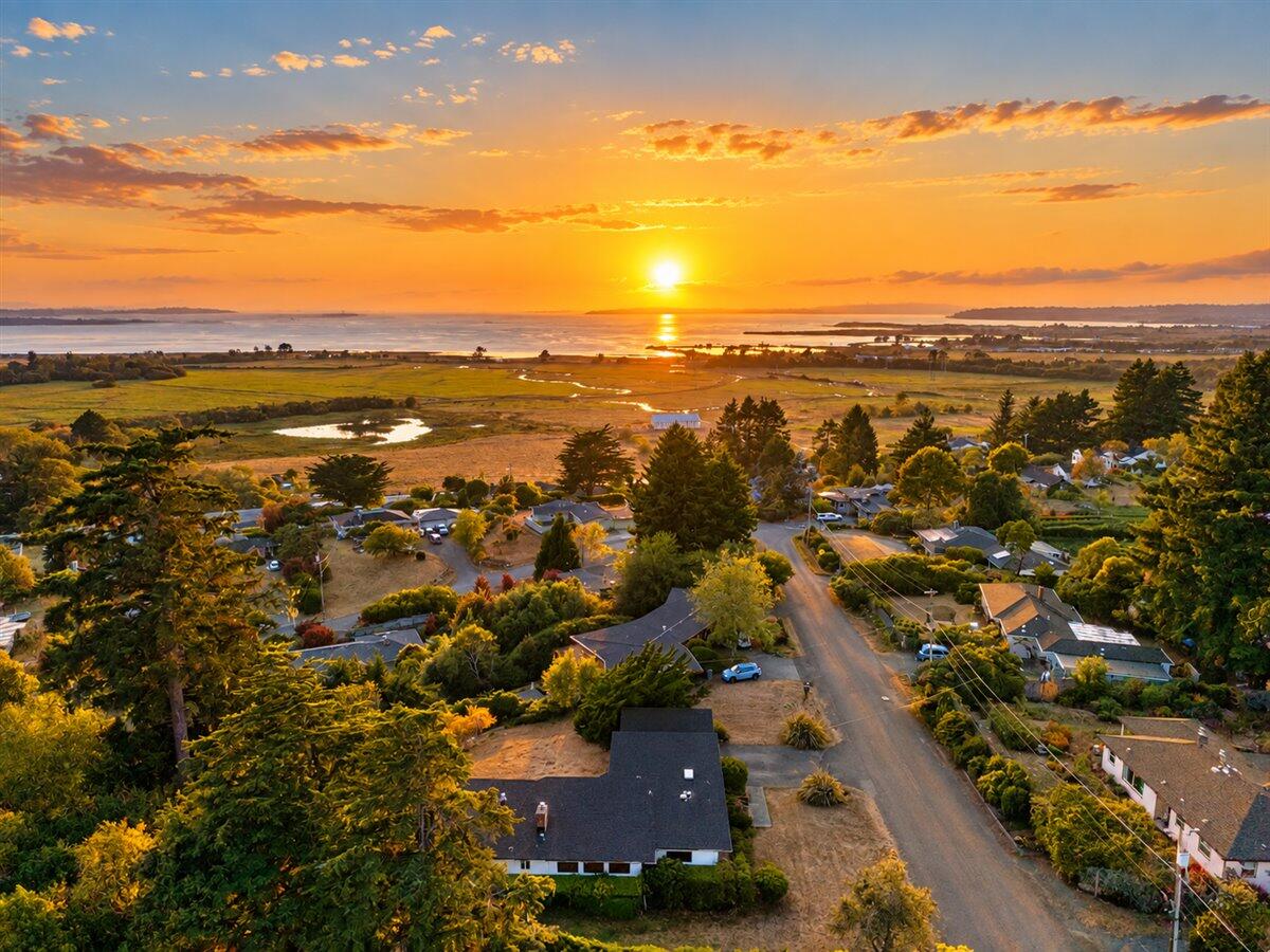 Aerial view of homes and wetlands beside a bay at sunset, with the sun reflecting on the water.