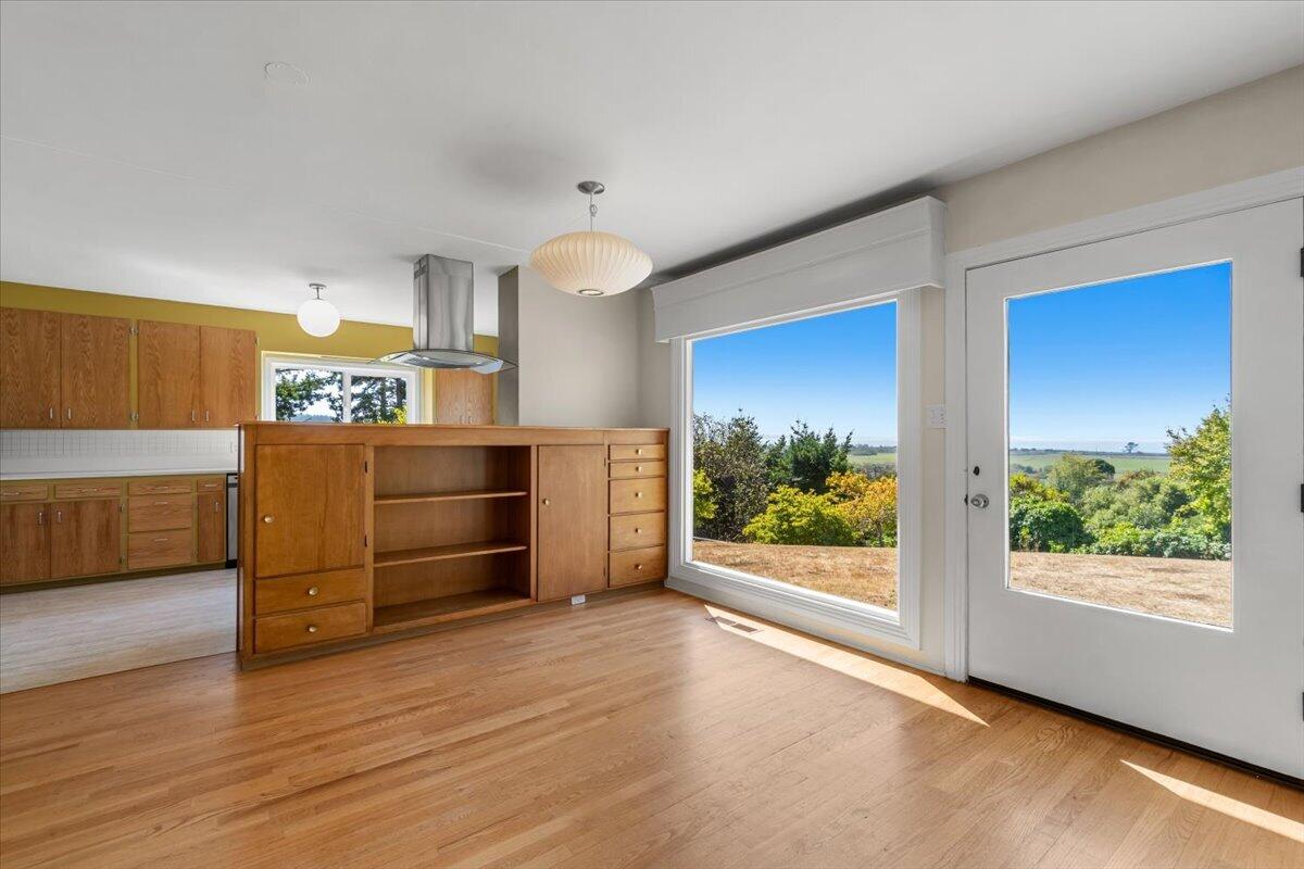 Kitchen with wood cabinetry, hardwood floors, and large windows overlooking greenery and distant water.
