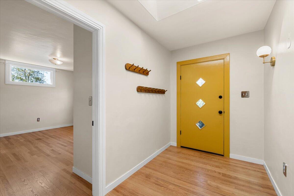 Entry foyer with a mustard-yellow front door and wooden coat racks.