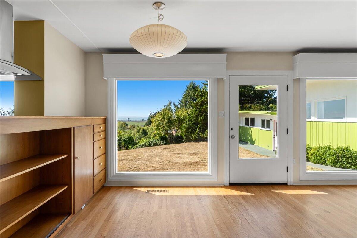 Vacant kitchen with built-in wooden shelving and large windows overlooking trees, lawn, and distant water.