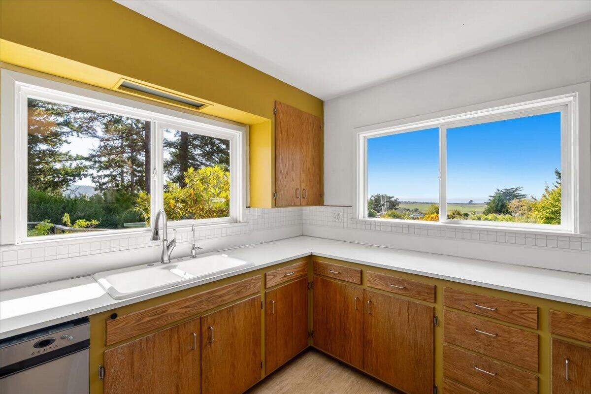 Kitchen with wood cabinets, a corner sink, and large windows overlooking a coastal landscape.