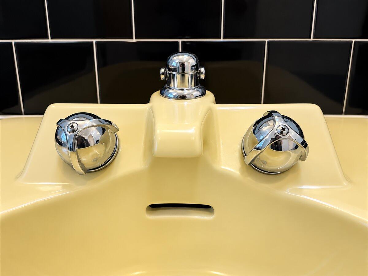 Cream bathroom sink with chrome faucet handles against a black tile backsplash.