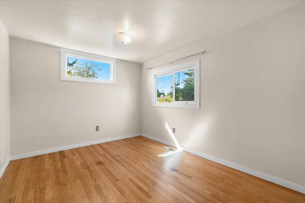 Vacant bedroom with hardwood floors and two windows.
