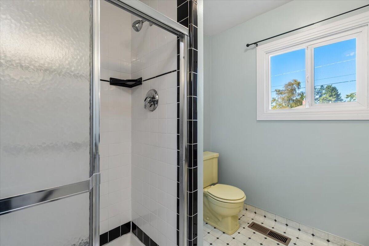 Bathroom with a glass-enclosed tiled shower, toilet, and window overlooking trees.