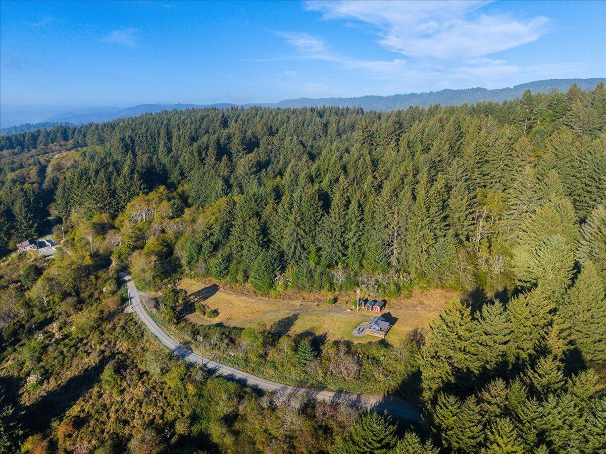 Aerial view of a forested rural property, with a road curving past a clearing and small outbuildings.