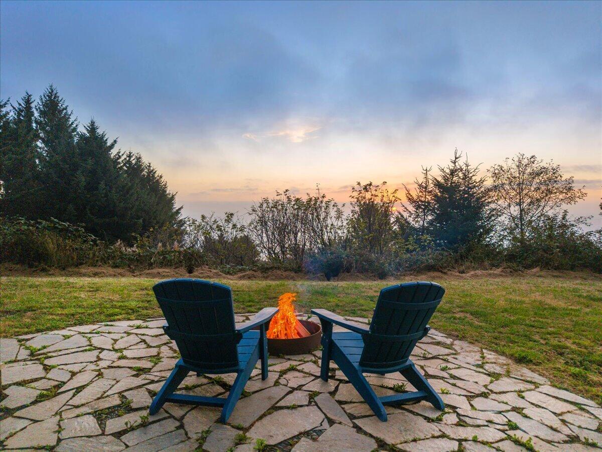 Stone patio with two Adirondack chairs around a fire pit at dusk.