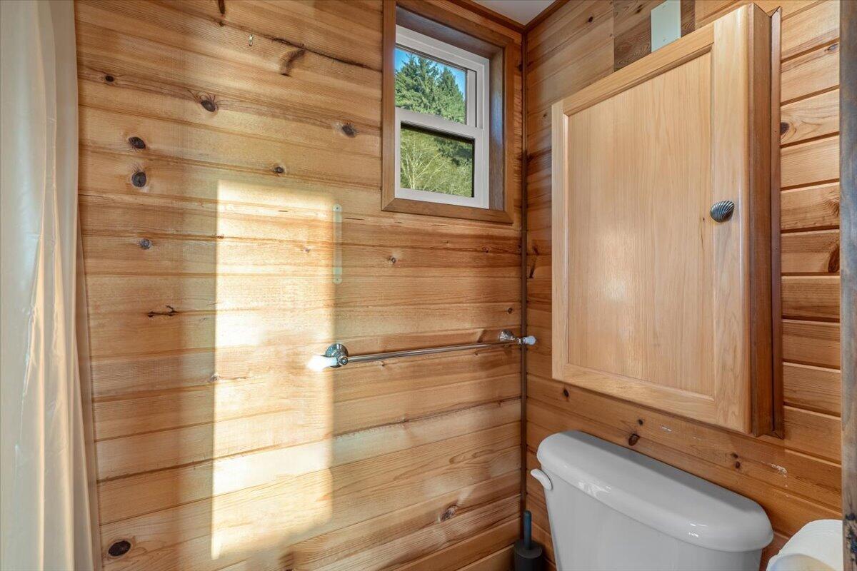 Wood-paneled bathroom with a wall cabinet, toilet, and small window.