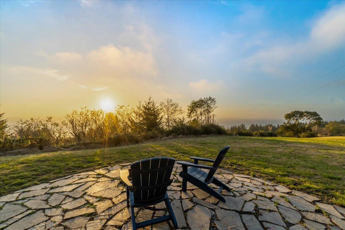 Grassy backyard with Adirondack chairs on a flagstone patio facing the low sun.