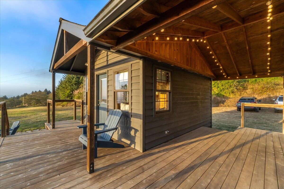 Covered wooden deck with string lights, Adirondack chairs, and views of a grassy yard.