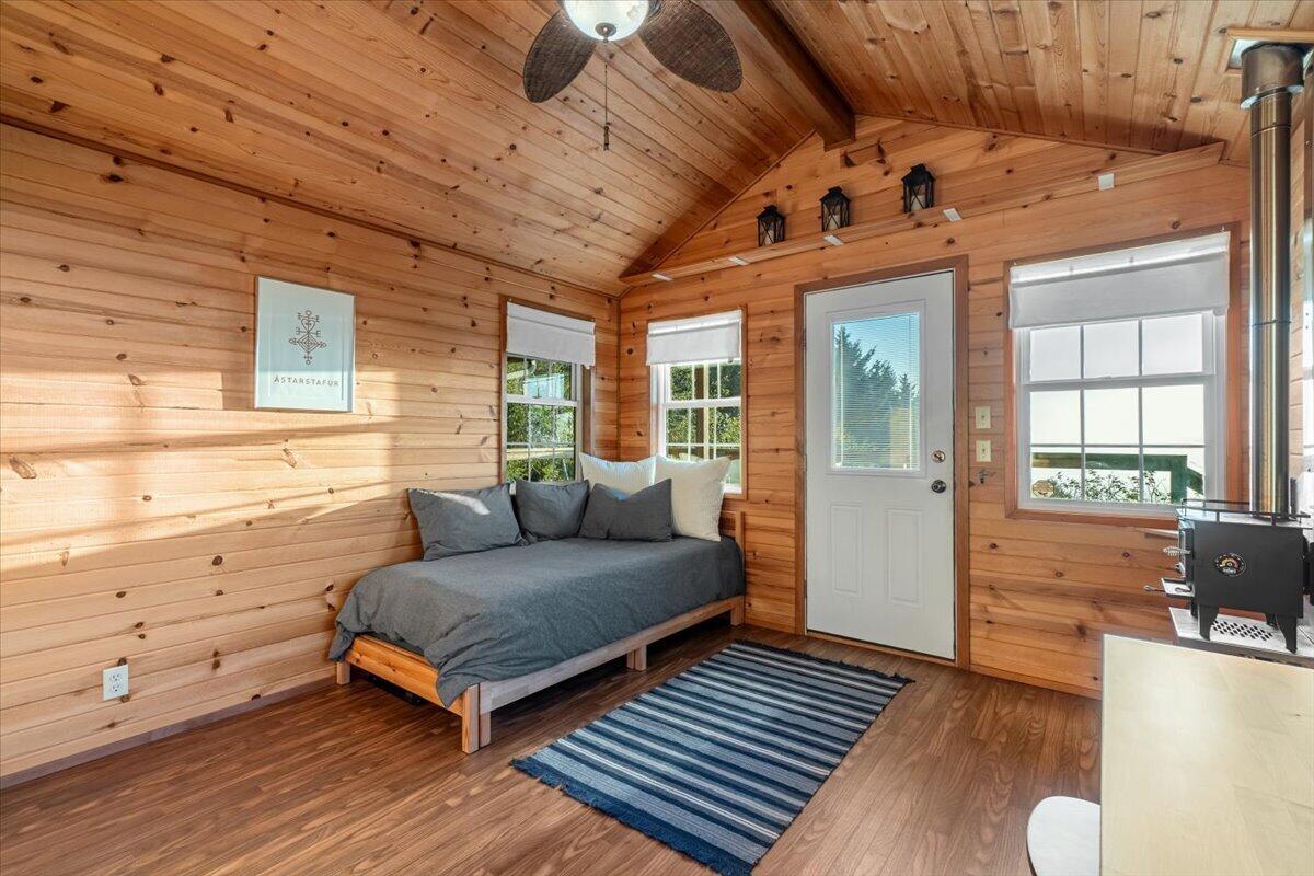 Wood-paneled bedroom with a gray daybed, striped rug, and black wood stove.