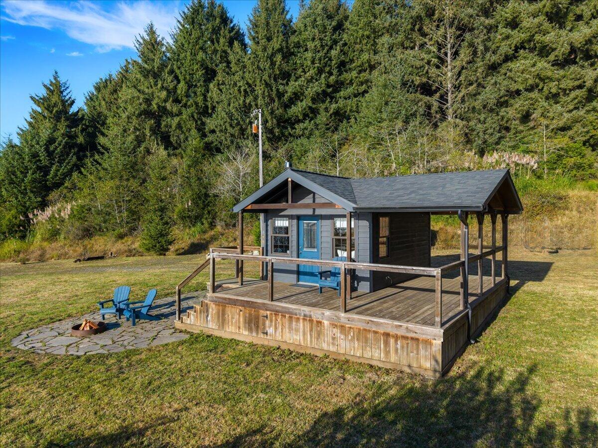 Small cabin with a wraparound deck and blue Adirondack chairs in a forest clearing.