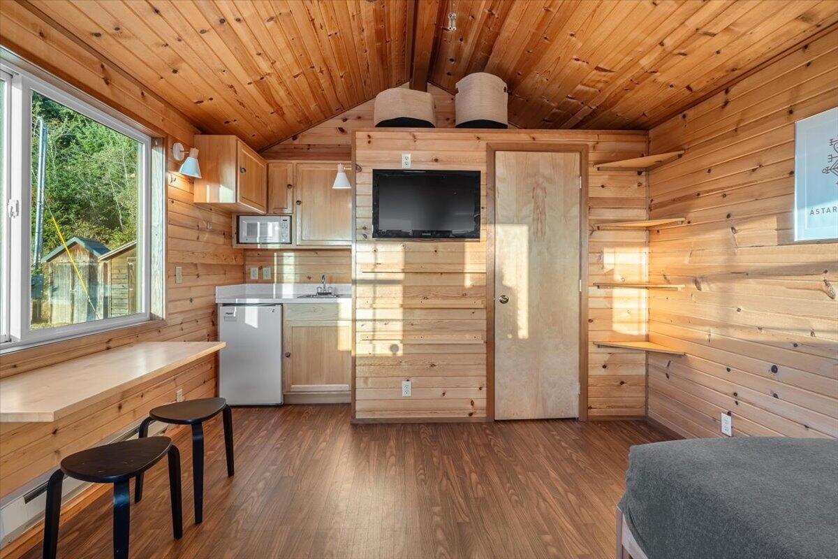Compact wood-paneled cabin interior with a kitchenette, built-in shelves, and a large window.
