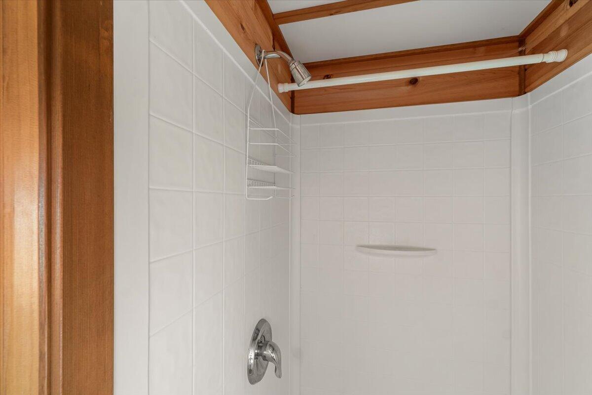 Tiled shower with chrome fixtures, a wire caddy, and exposed wooden ceiling beams.