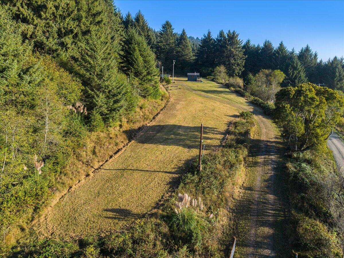 Aerial view of a wooded property with a long grassy clearing, dirt track, and small outbuilding.