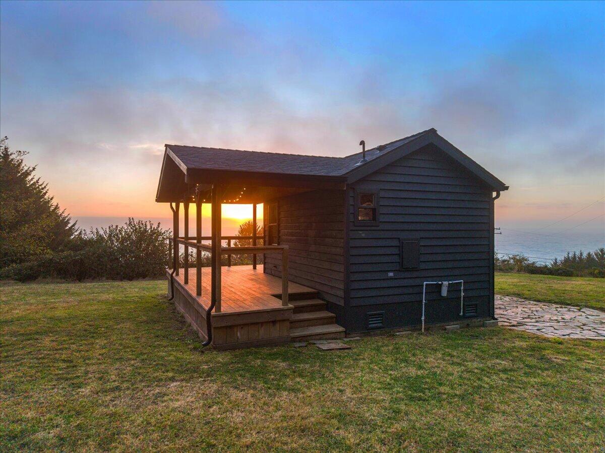 Coastal cabin with a covered porch overlooking the ocean at sunset.