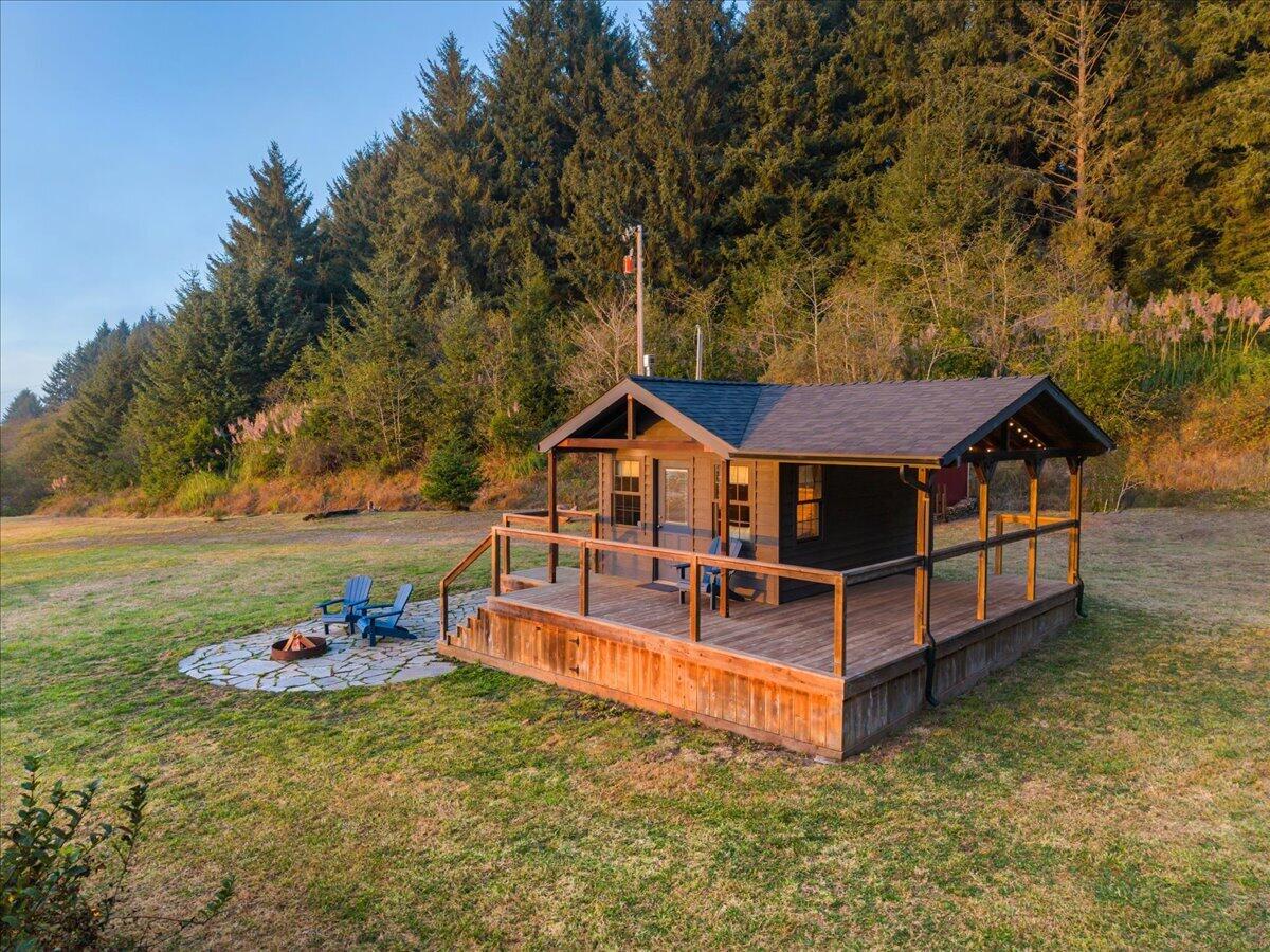 Wood-sided cabin with wraparound deck and stone fire-pit patio in a forest clearing.