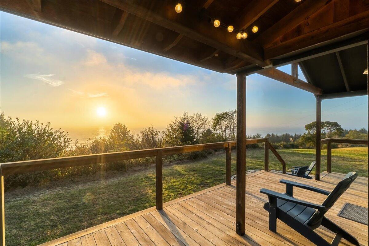 Covered wooden deck with Adirondack chairs overlooking the ocean at sunset.