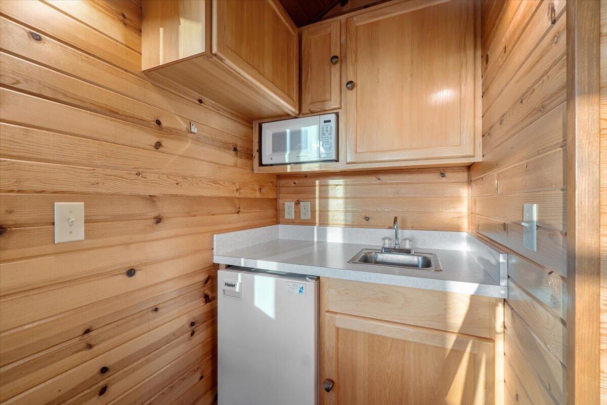 Compact pine-paneled kitchen with a sink, microwave, and small refrigerator.