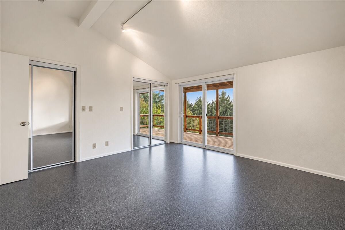 Vacant bedroom with vaulted ceiling and sliding glass doors to a wooded deck.