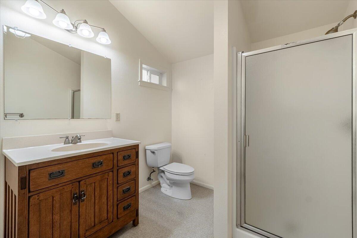 Bathroom with a wood vanity, wide mirror, toilet, and glass shower enclosure.